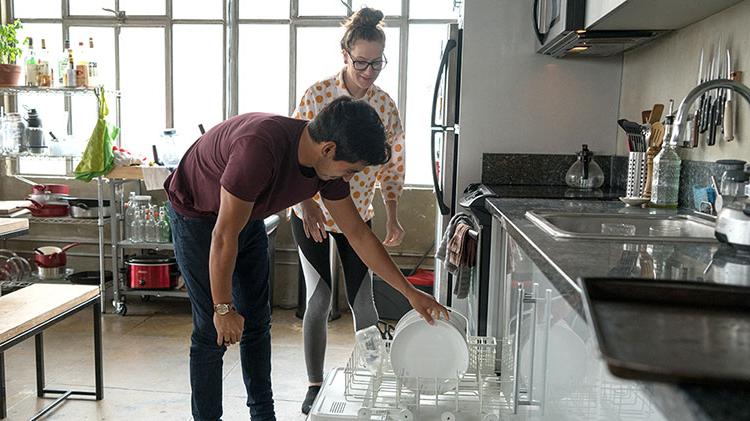 Couple loading dishwasher and discussing appliance maintenance.