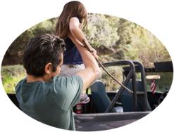 A father guides his daughter into a back-seat safety restraint